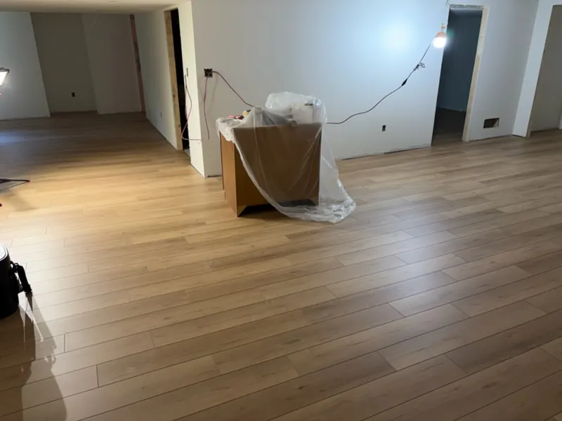 Open living area with new light wood-look plank flooring and a window glowing at the far end
